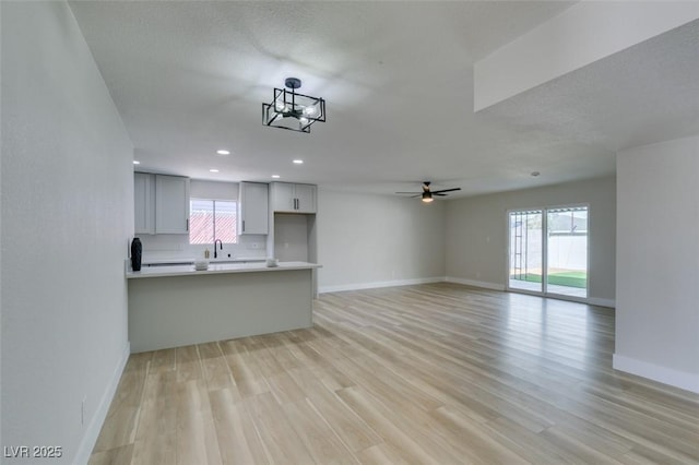 unfurnished living room with ceiling fan with notable chandelier, recessed lighting, light wood-style floors, and baseboards