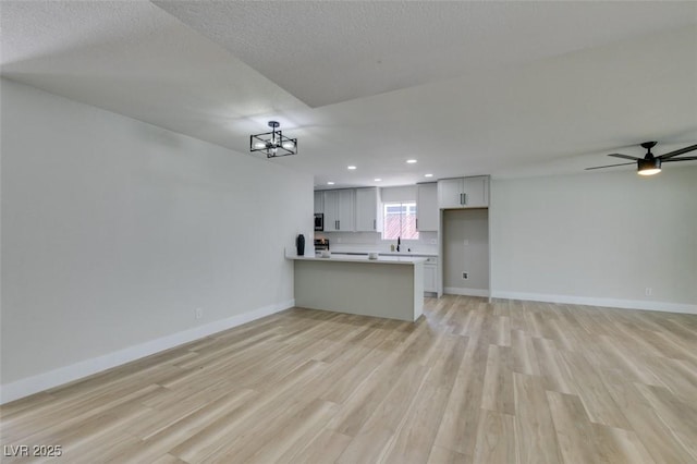 unfurnished living room featuring light wood-type flooring, ceiling fan with notable chandelier, a textured ceiling, recessed lighting, and baseboards