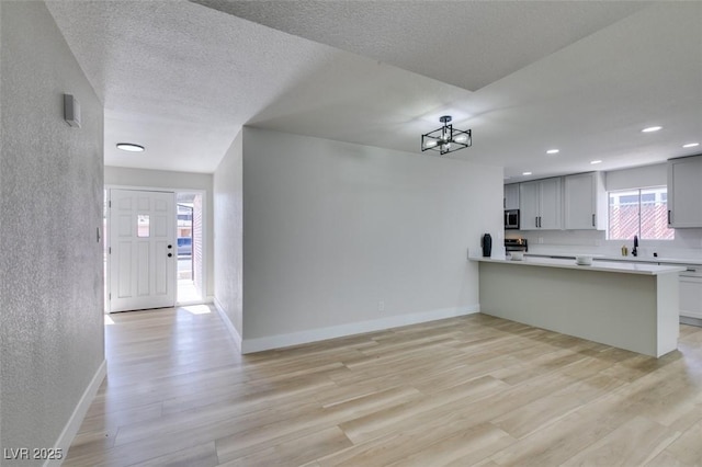 kitchen featuring baseboards, light countertops, light wood-type flooring, appliances with stainless steel finishes, and a textured ceiling