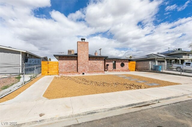 view of front of house with a gate, fence, a chimney, concrete driveway, and brick siding