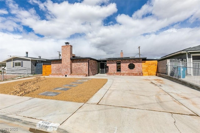 view of front of property with roof mounted solar panels, brick siding, a chimney, and fence