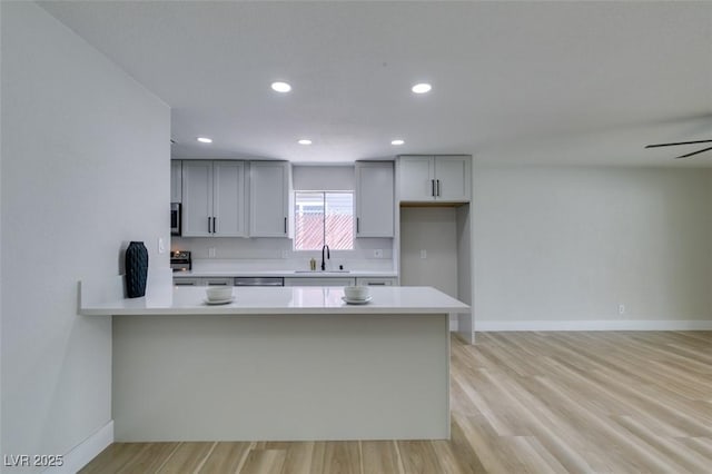 kitchen featuring light wood-type flooring, a sink, a peninsula, light countertops, and baseboards