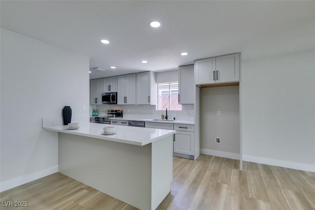 kitchen with light wood-type flooring, a sink, recessed lighting, appliances with stainless steel finishes, and light countertops