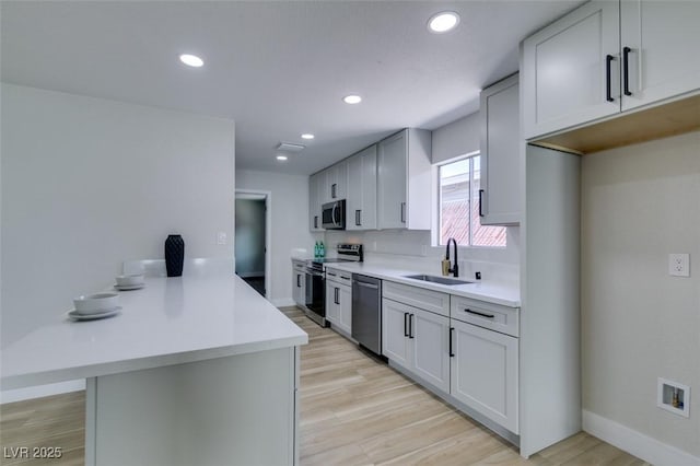 kitchen with light wood-type flooring, a sink, stainless steel appliances, a peninsula, and light countertops