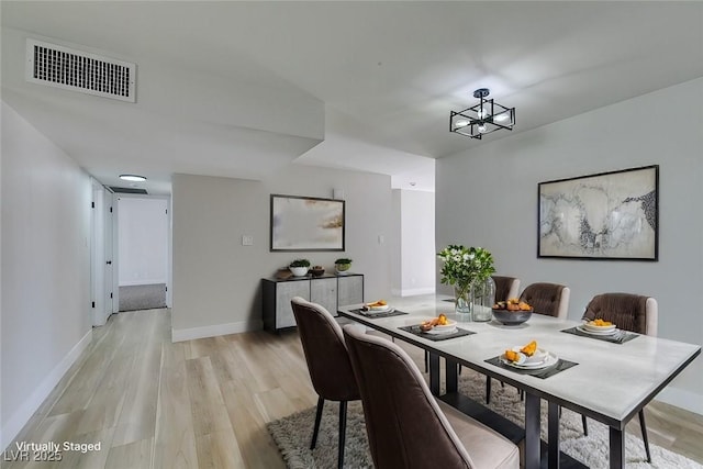 dining area with light wood finished floors, visible vents, a notable chandelier, and baseboards