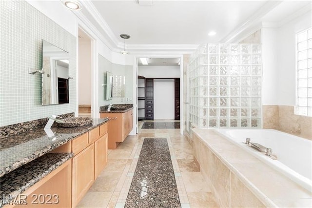 full bathroom with two vanities, a garden tub, tile patterned flooring, crown molding, and tile walls