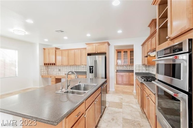 kitchen featuring dark countertops, light brown cabinetry, appliances with stainless steel finishes, a sink, and under cabinet range hood