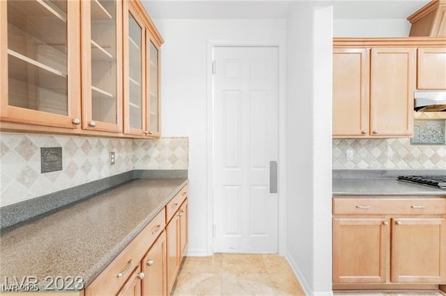 kitchen featuring light tile patterned floors, tasteful backsplash, baseboards, glass insert cabinets, and under cabinet range hood