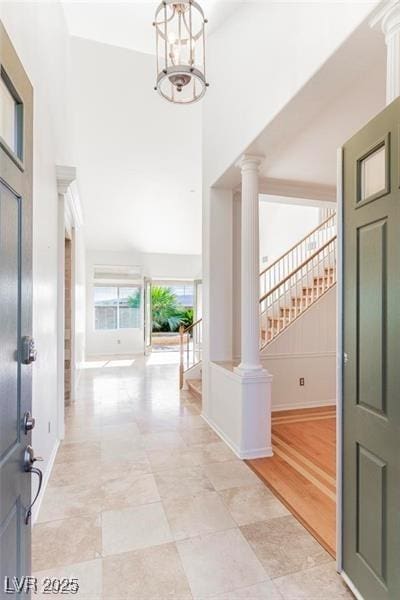 foyer entrance with a chandelier, a towering ceiling, baseboards, stairs, and ornate columns