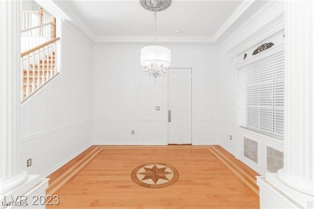 unfurnished dining area featuring an inviting chandelier, decorative columns, light wood-style flooring, and crown molding