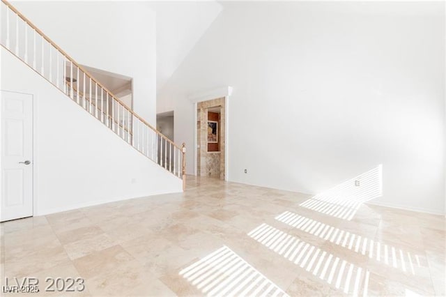 unfurnished living room featuring baseboards, stairway, and a towering ceiling