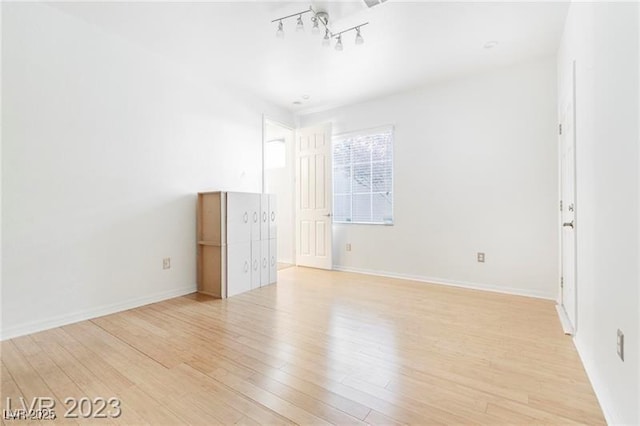 empty room with rail lighting, baseboards, and light wood finished floors