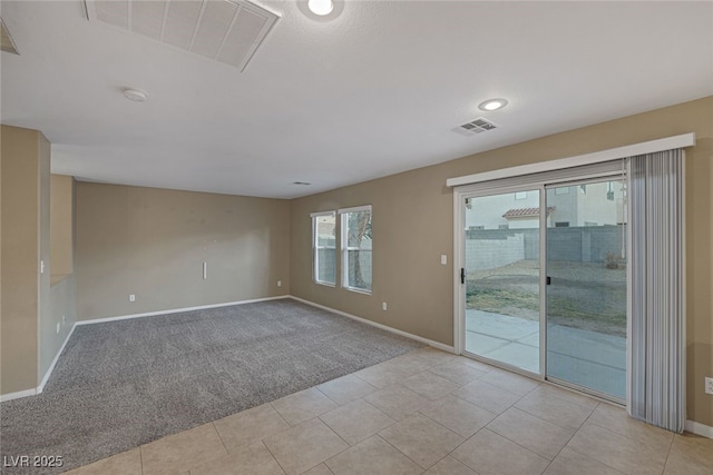 spare room with light tile patterned floors, visible vents, baseboards, and light colored carpet