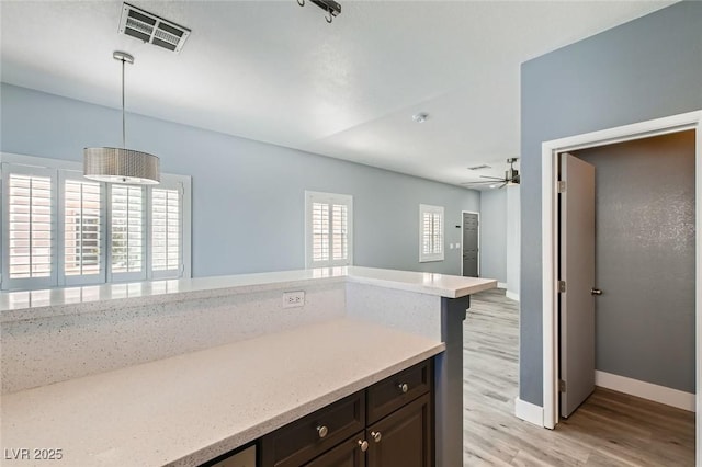 kitchen with light wood-type flooring, visible vents, baseboards, ceiling fan, and hanging light fixtures