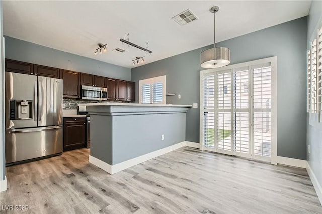 kitchen with visible vents, light wood finished floors, stainless steel appliances, hanging light fixtures, and dark brown cabinetry