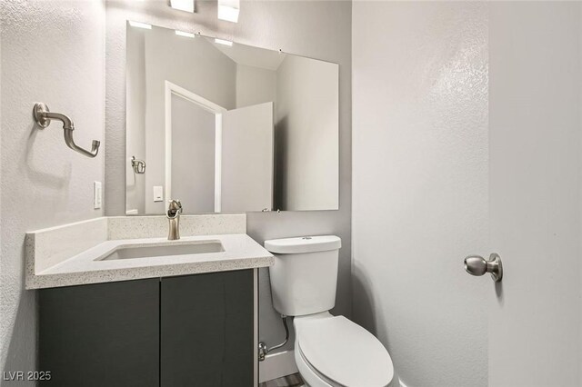 half bath with toilet, vanity, and a textured wall