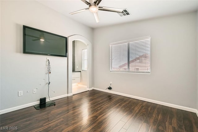 empty room with visible vents, ceiling fan, baseboards, dark wood-style floors, and arched walkways