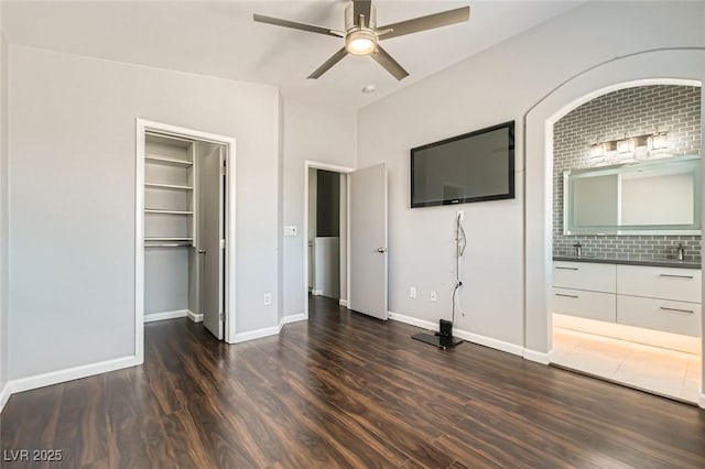 unfurnished bedroom featuring a walk in closet, dark wood-type flooring, baseboards, and connected bathroom