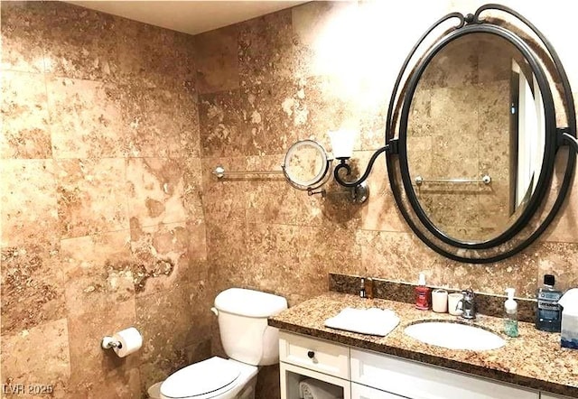 bathroom with a sink, double vanity, toilet, and tile walls