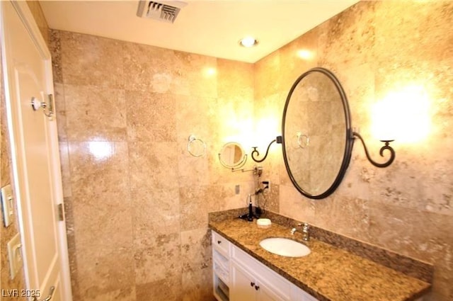 bathroom with vanity, visible vents, and tile walls