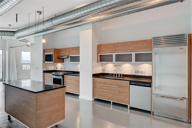 kitchen with modern cabinets, under cabinet range hood, a sink, dark countertops, and built in appliances