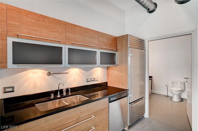 kitchen with a sink, dark countertops, built in fridge, glass insert cabinets, and dishwasher