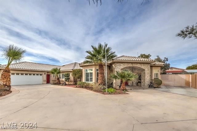 mediterranean / spanish-style home featuring a tile roof, concrete driveway, fence, a garage, and stone siding