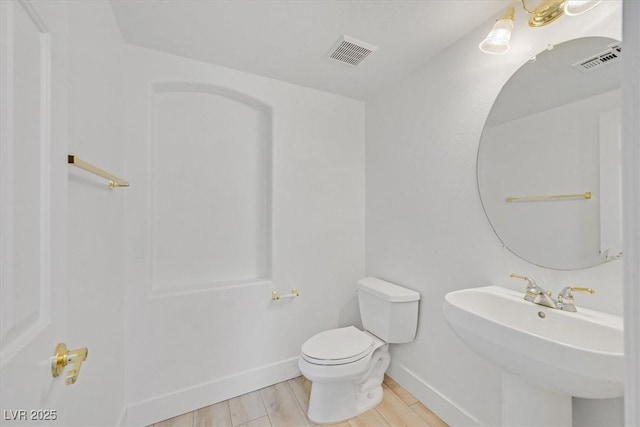 half bath with visible vents, a sink, toilet, and wood finished floors