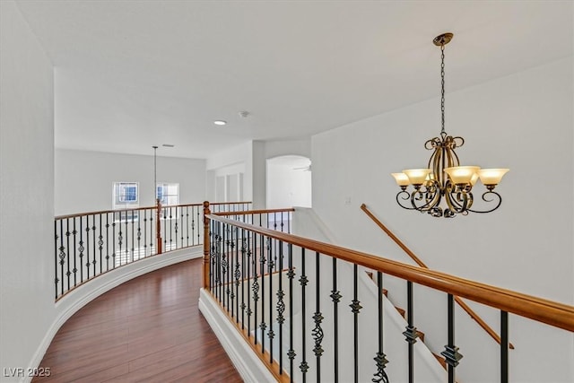 hall with dark wood-style floors, baseboards, arched walkways, a notable chandelier, and an upstairs landing