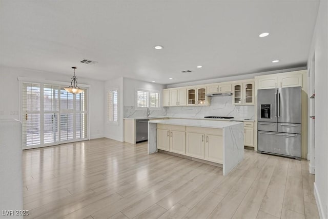 kitchen featuring visible vents, glass insert cabinets, light wood-type flooring, light countertops, and appliances with stainless steel finishes