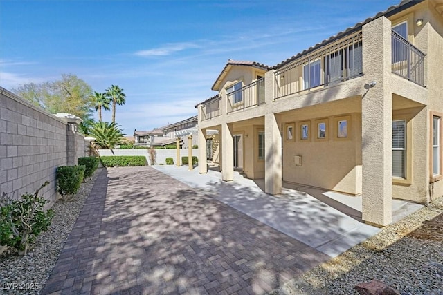 back of house featuring stucco siding, a fenced backyard, a residential view, a balcony, and a patio area