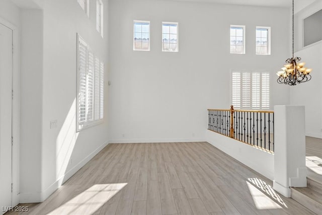 spare room with a wealth of natural light, an inviting chandelier, and wood finished floors