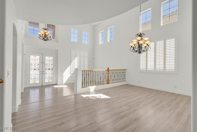 foyer with light wood-style flooring, a towering ceiling, french doors, baseboards, and a chandelier