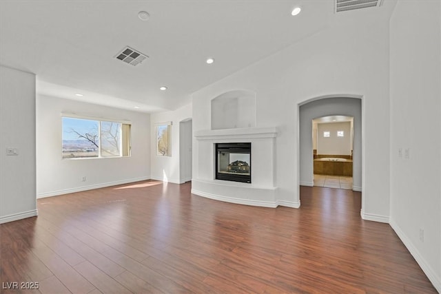 unfurnished living room featuring recessed lighting, visible vents, arched walkways, and wood finished floors