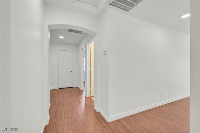 corridor featuring baseboards, arched walkways, visible vents, and light wood-style flooring