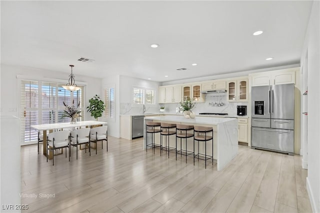 kitchen featuring light wood finished floors, visible vents, under cabinet range hood, stainless steel appliances, and a sink