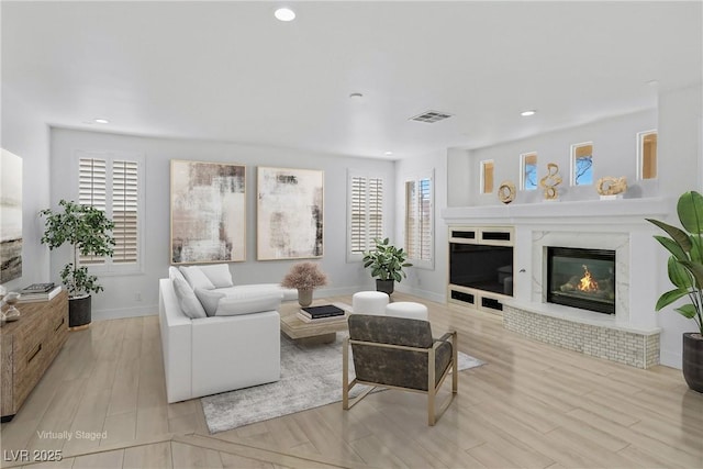 living room with a glass covered fireplace, wood finished floors, a healthy amount of sunlight, and visible vents