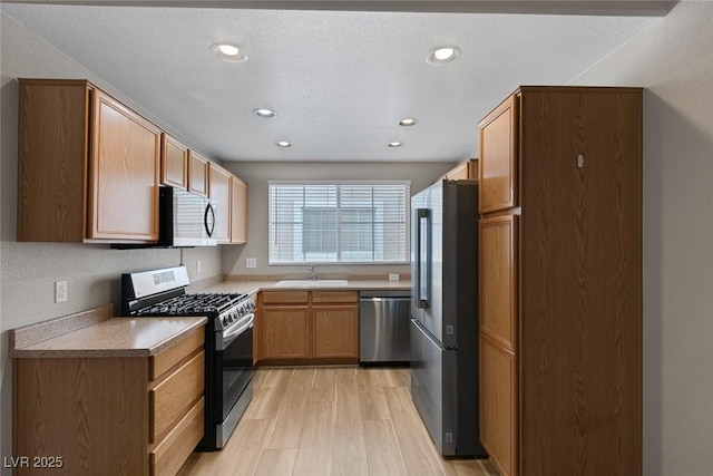 kitchen featuring brown cabinets, recessed lighting, appliances with stainless steel finishes, a sink, and light wood-type flooring