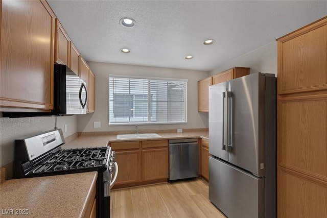 kitchen featuring a textured ceiling, a sink, light wood-style floors, light countertops, and appliances with stainless steel finishes