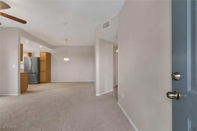 unfurnished living room featuring a ceiling fan, visible vents, light carpet, and baseboards