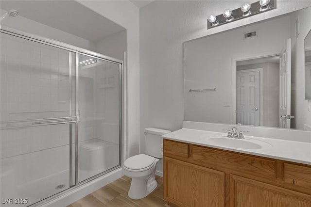 full bathroom featuring toilet, wood finished floors, vanity, visible vents, and a shower stall