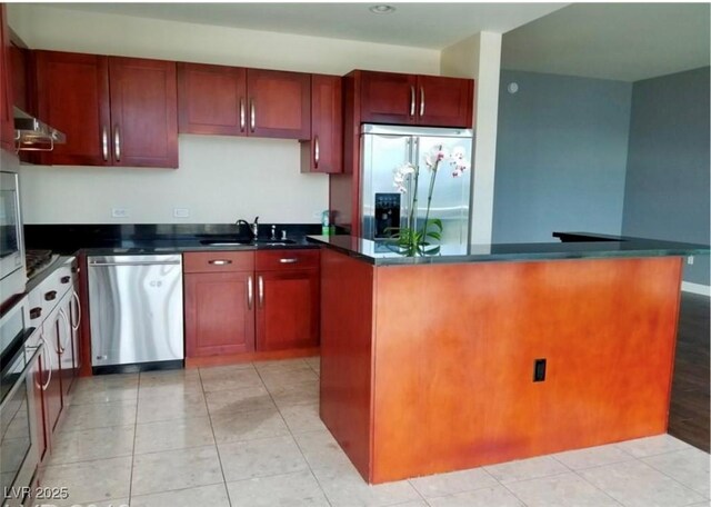 kitchen with light tile patterned floors, dark countertops, appliances with stainless steel finishes, a sink, and dark brown cabinets