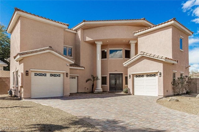 mediterranean / spanish-style home featuring a garage, a tile roof, decorative driveway, and stucco siding