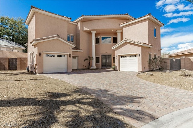 view of front of property with an attached garage, a tiled roof, decorative driveway, a gate, and stucco siding