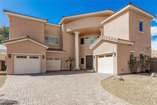 mediterranean / spanish-style home with decorative driveway, an attached garage, a tile roof, and stucco siding