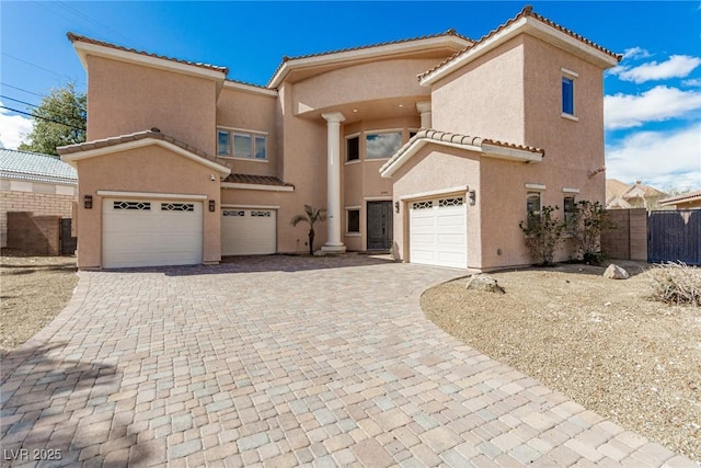 mediterranean / spanish home featuring a garage, a tiled roof, fence, decorative driveway, and stucco siding