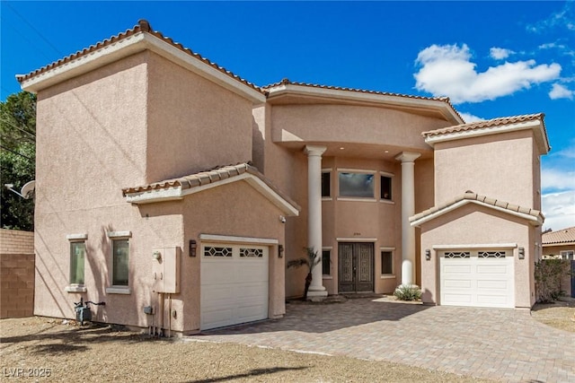 mediterranean / spanish home with an attached garage, a tiled roof, decorative driveway, and stucco siding