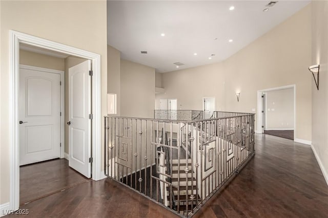 corridor with recessed lighting, wood finished floors, a towering ceiling, and baseboards