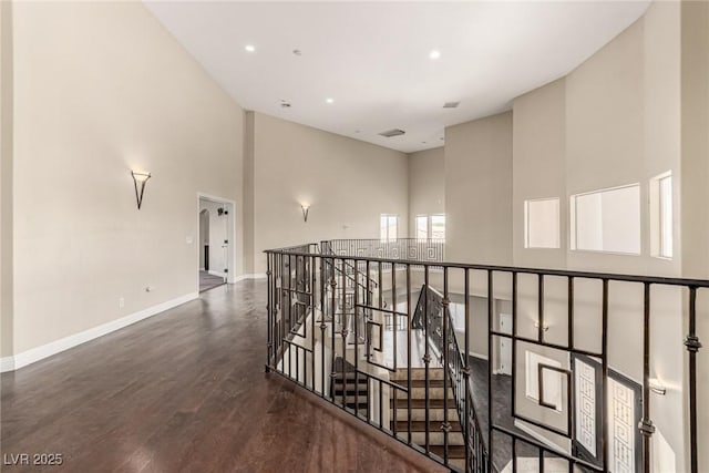 hallway featuring baseboards, wood finished floors, a high ceiling, an upstairs landing, and recessed lighting