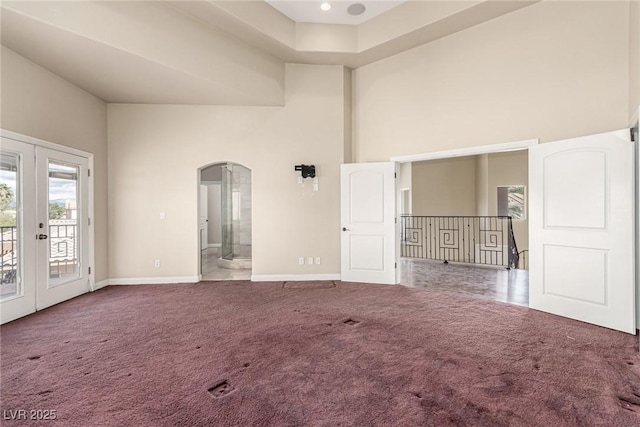 carpeted empty room with arched walkways, french doors, a towering ceiling, and baseboards